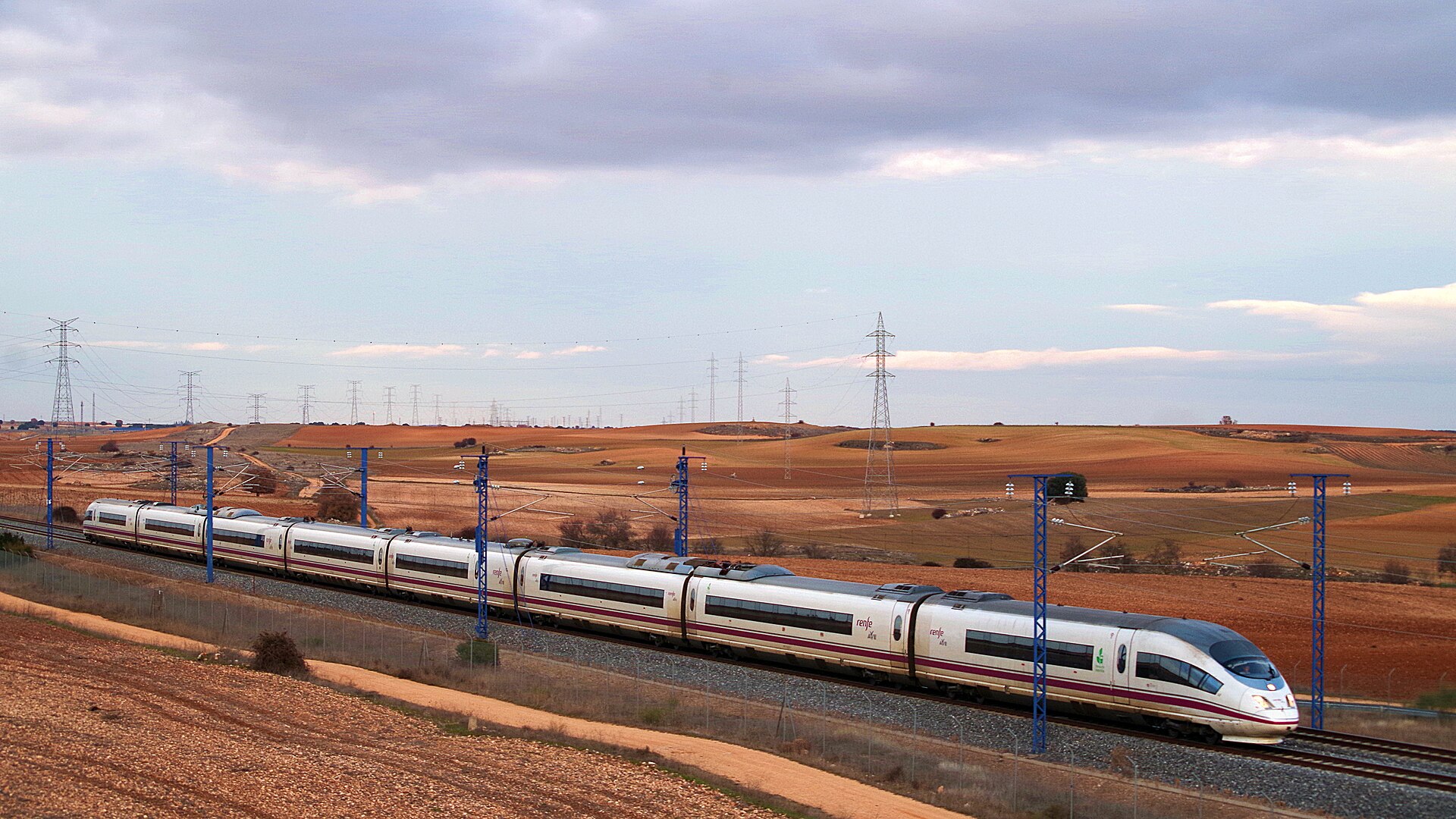 A Renfe AVE high speed train in white and grey livery on the line between Madrid and Barcelona, seen at an angle on a clear day.