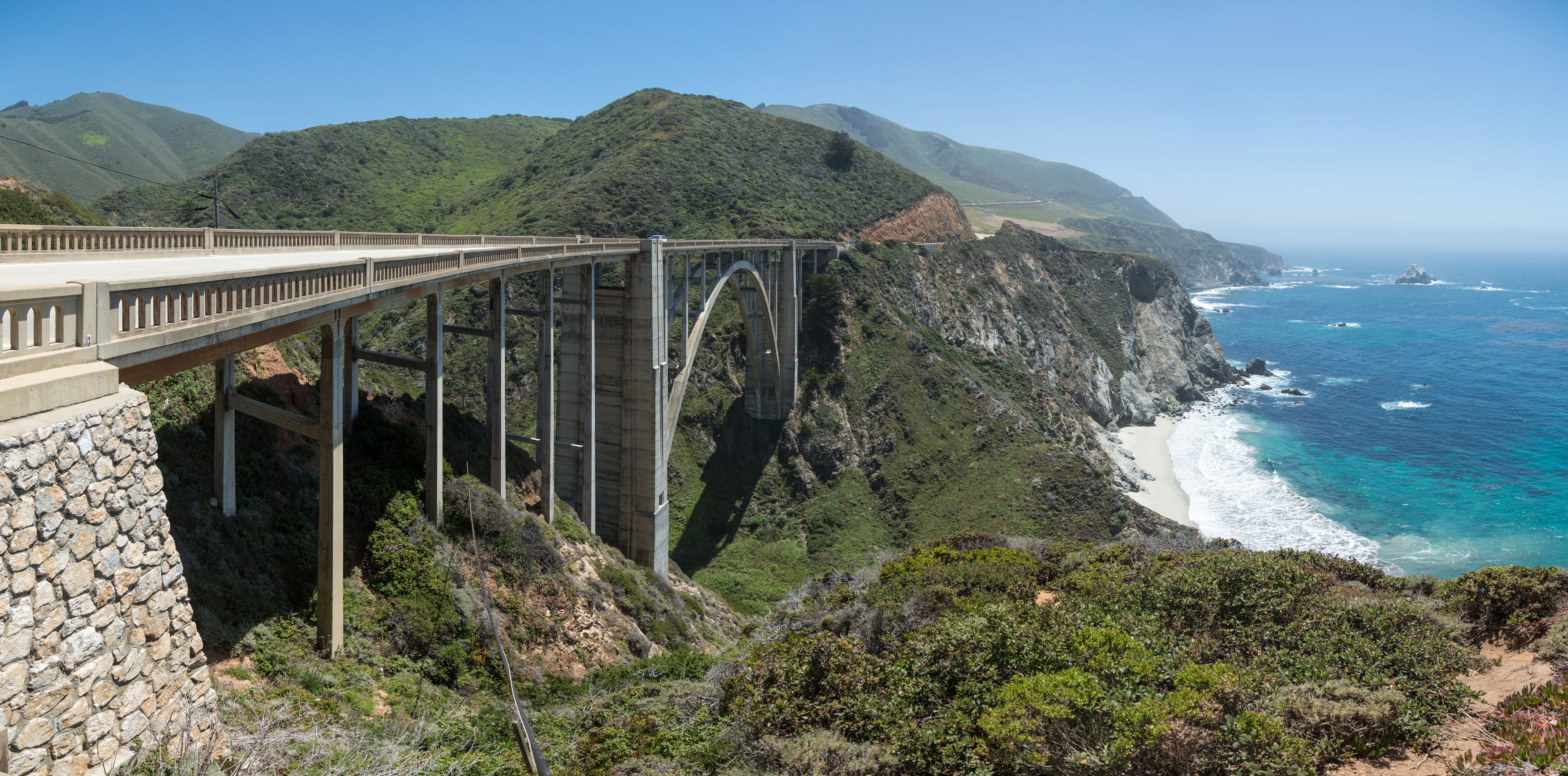 Bixby Creek Bridge on Highway 1 near Big Sur, its concrete arch spanning a steep coastal canyon with the Pacific Ocean beyond.