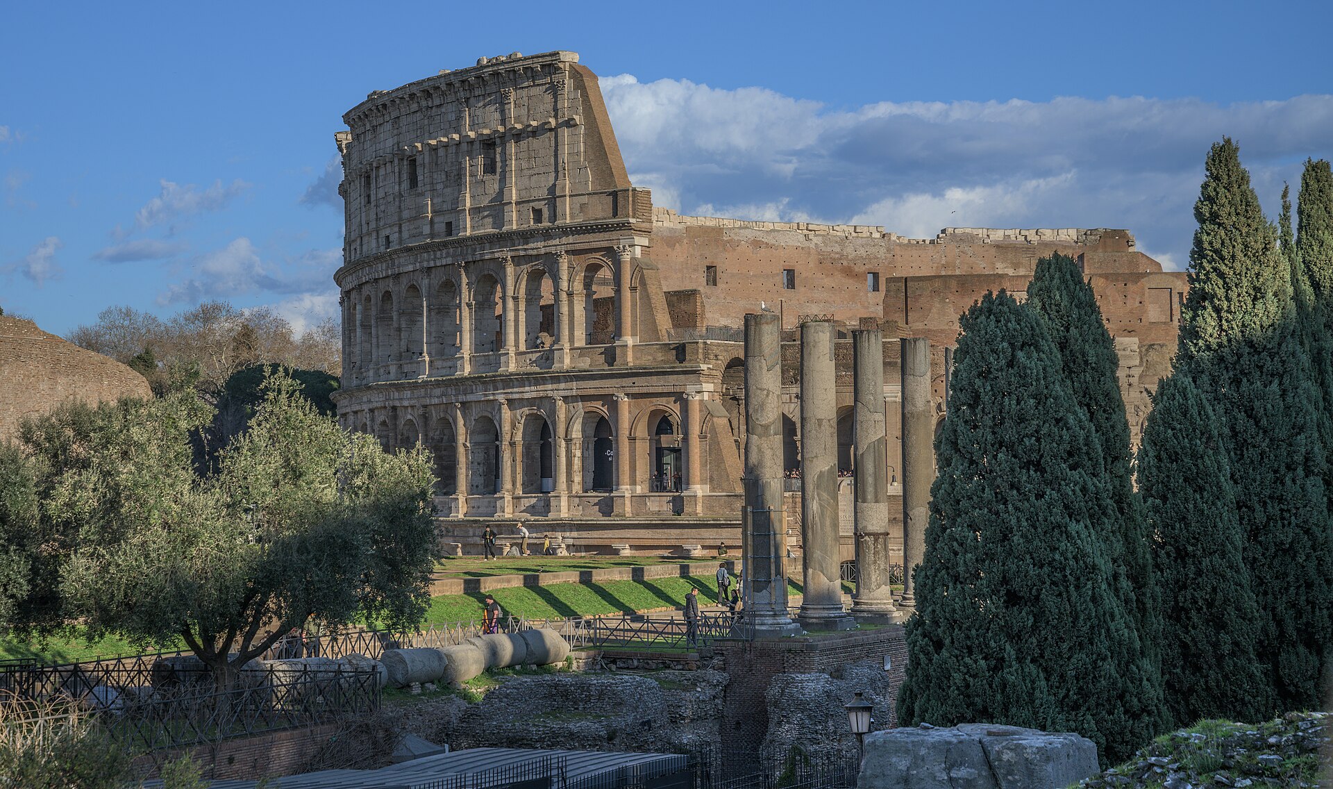 The Colosseum in Rome seen from above with the ruins of the Roman Forum stretching away behind it.