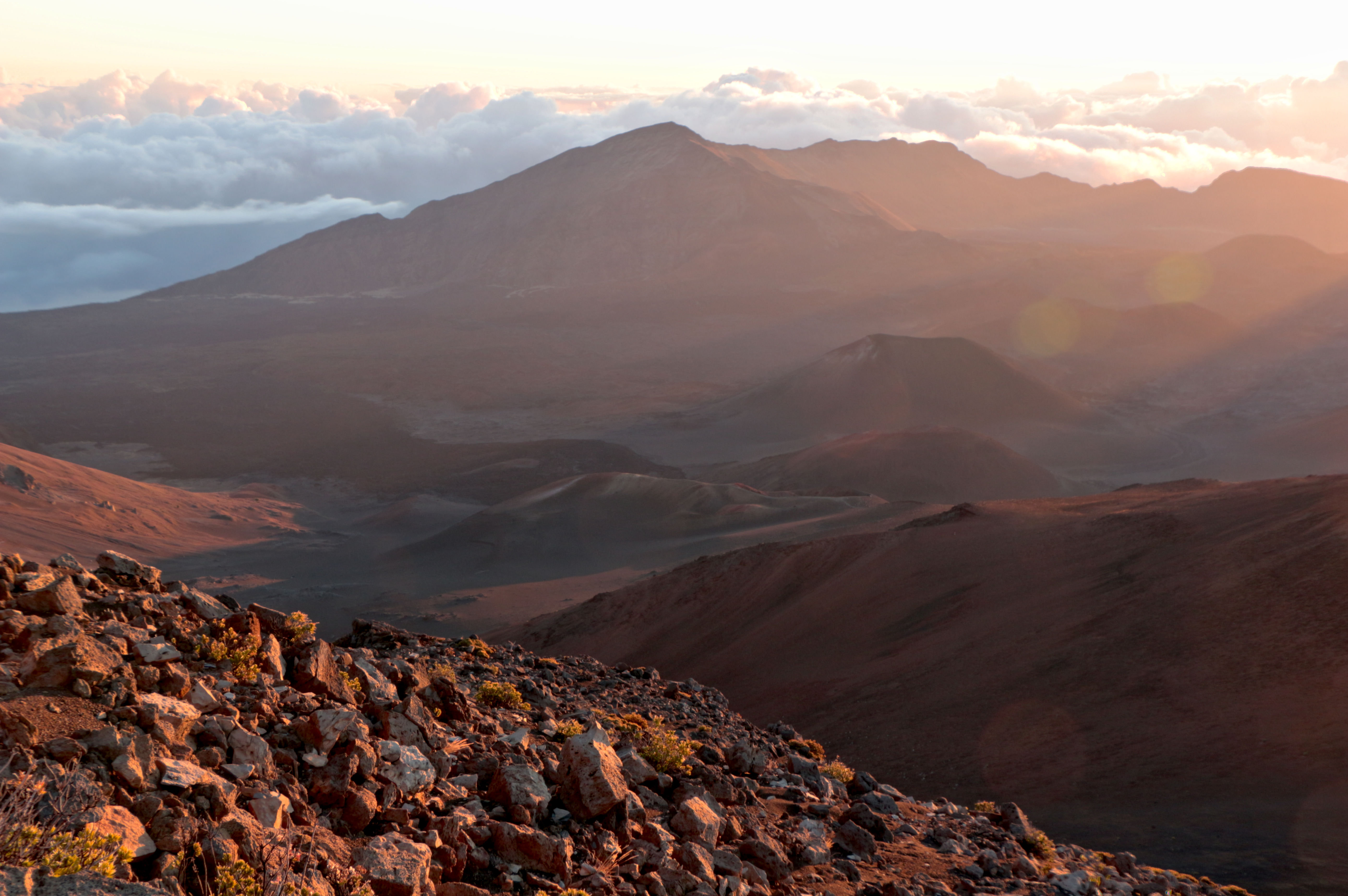 Early morning light over the crater of Haleakala volcano on Maui, layered clouds below the summit rim under a pale dawn sky.