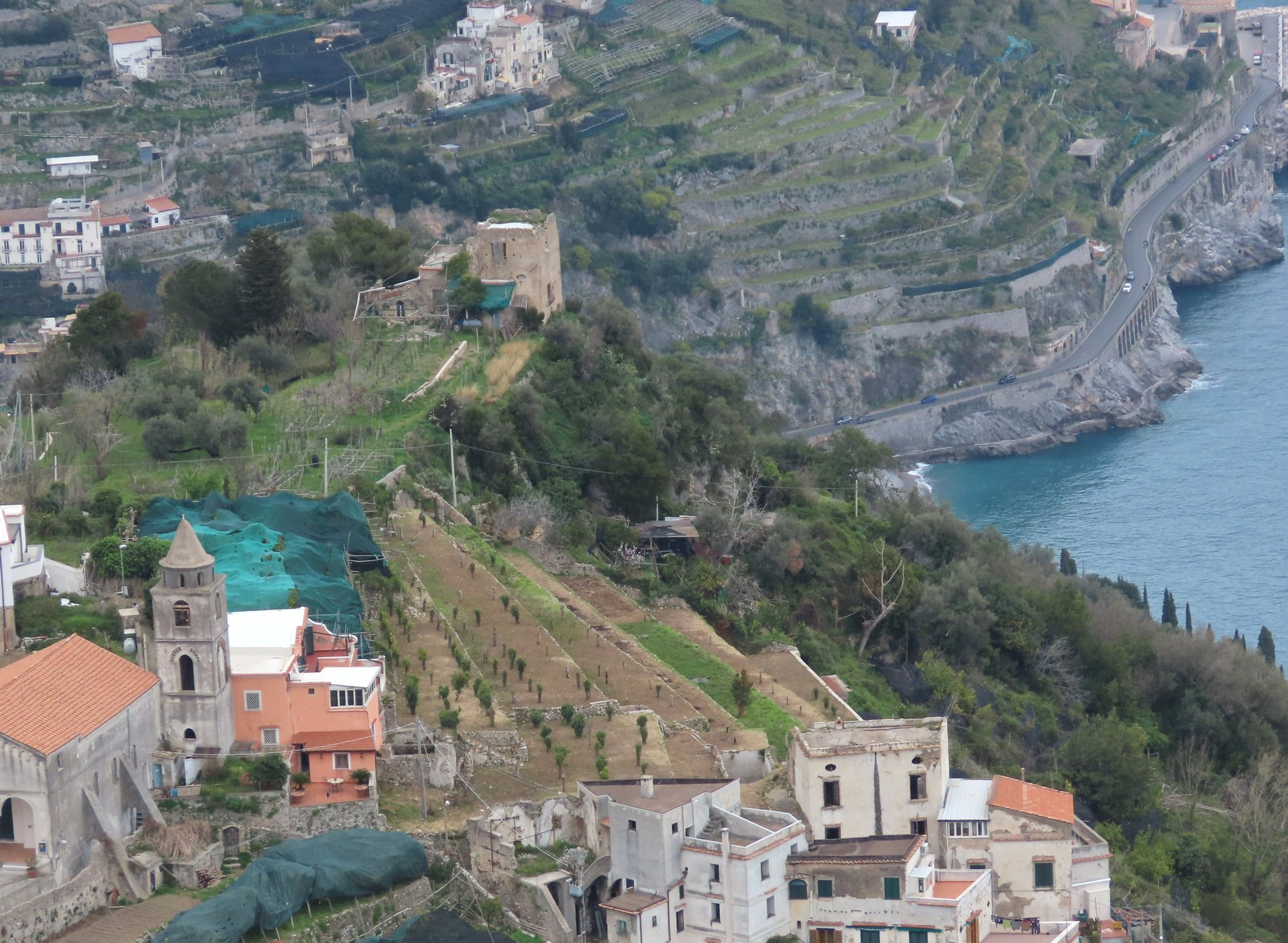 A tight bend on the Amalfi Coast road, cut into a steep terraced cliffside above the sea, with barely enough width for two vehicles.