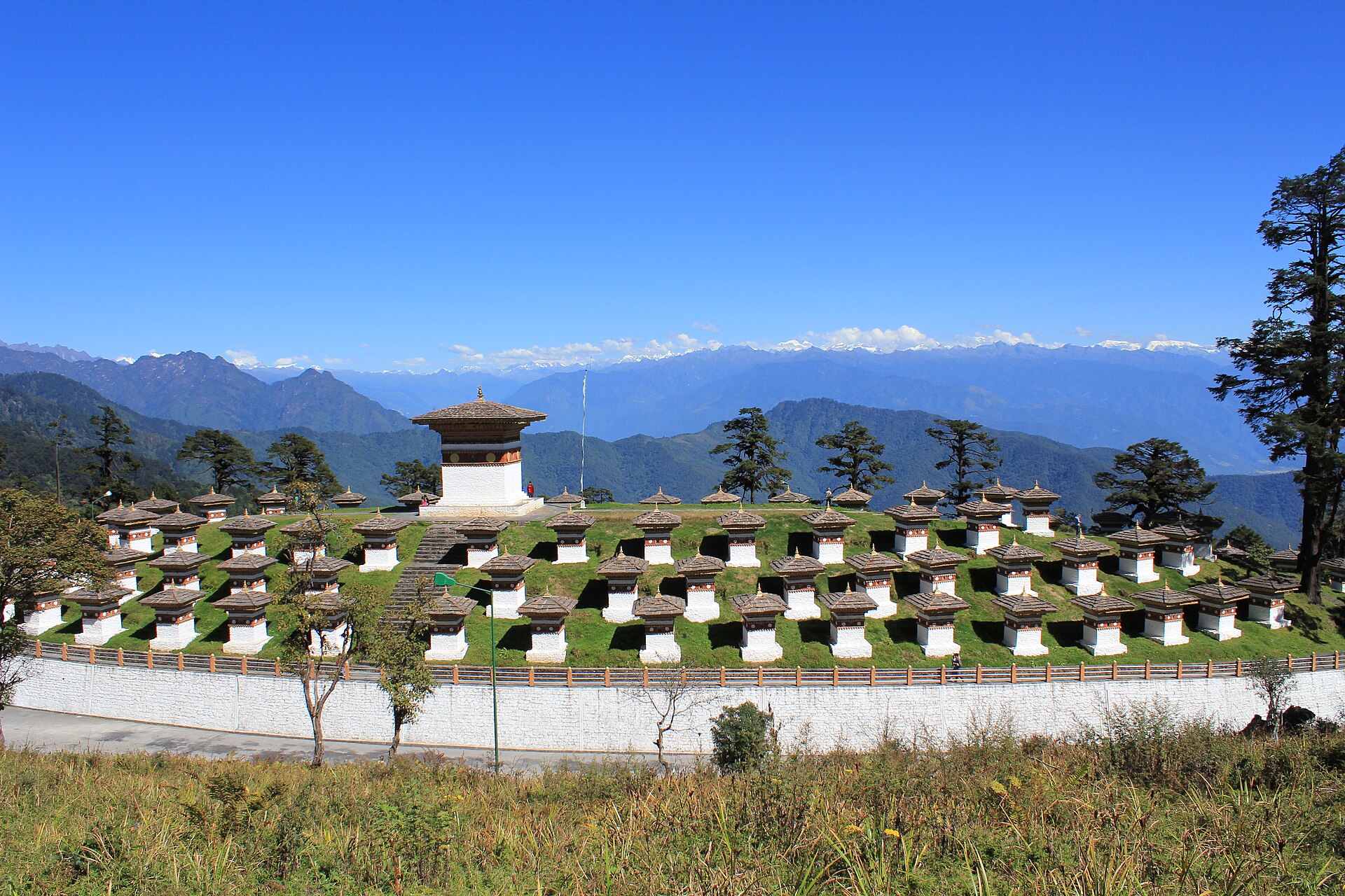 The 108 Druk Wangyal chortens standing in rows on the hillside at Dochula Pass, with prayer flags and forested slopes behind.