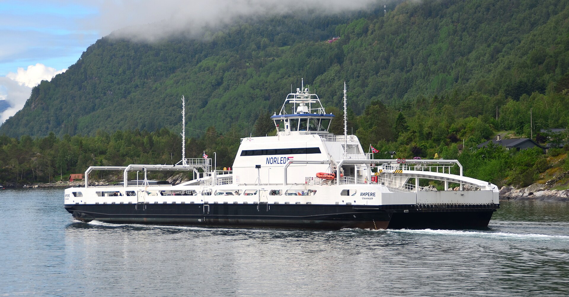 The electric car ferry Ampere crossing the Sognefjord near Lavik in western Norway, with low green hills and flat grey water around it.