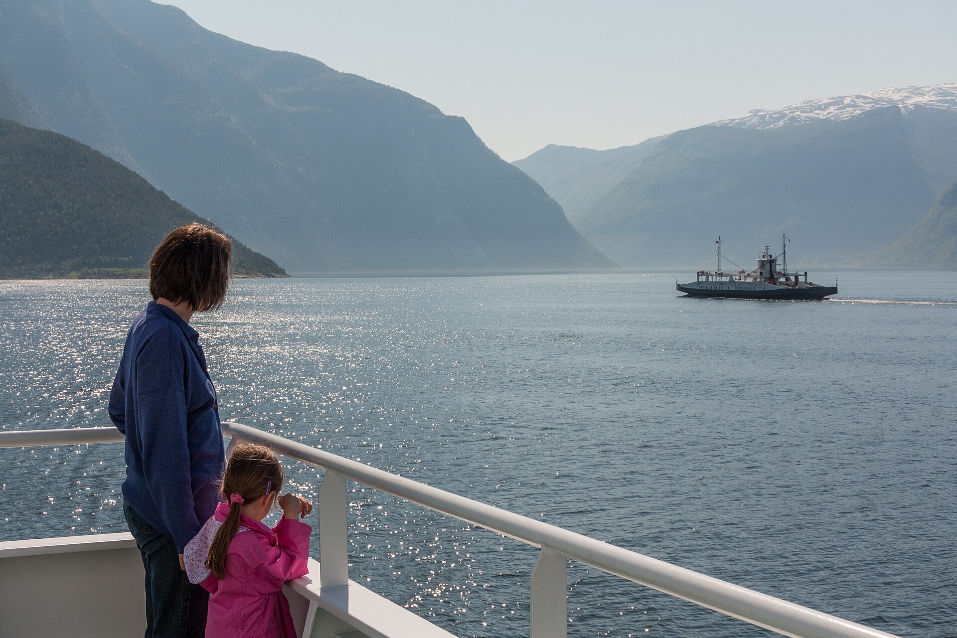 A car ferry approaching the quay at Mannheller on the Sognefjord in Norway, with steep green hillsides behind it.