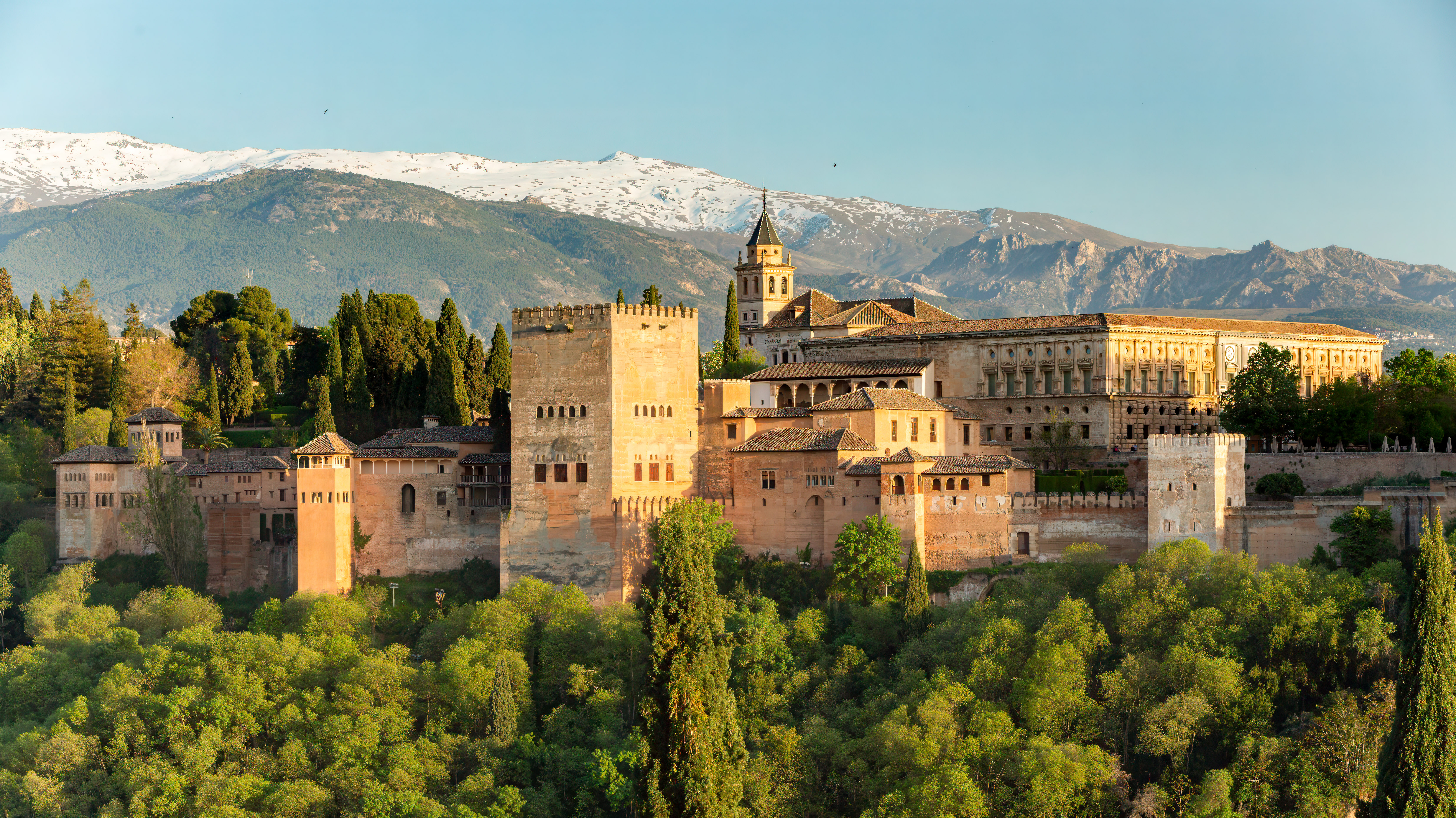 The Alhambra fortress and palace complex in Granada seen from across the valley at Mirador de San Nicolás, with the Sierra Nevada mountains behind it.