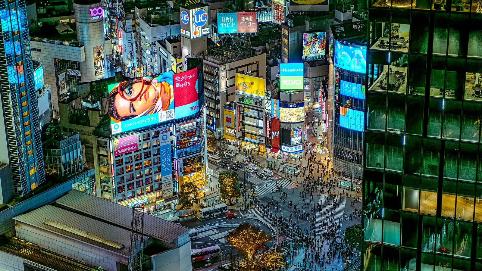 Shibuya Scramble Crossing seen from above at dusk, crowds mid-crossing under lit billboards.