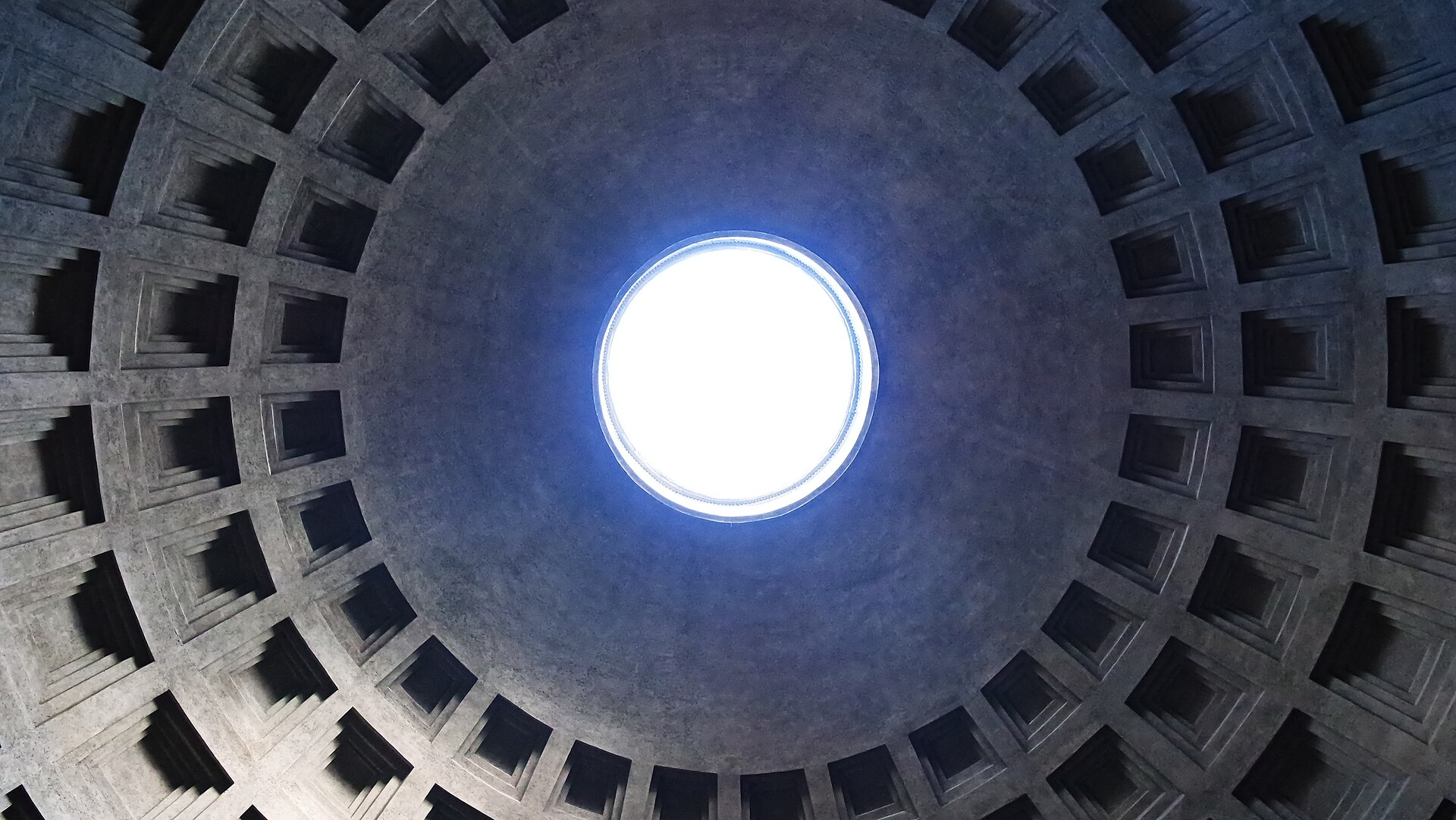 The coffered dome of the Pantheon in Rome seen from inside, with daylight falling through the circular oculus at its centre.