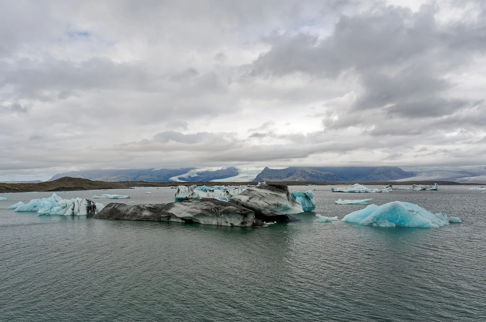 Icebergs floating in Jokulsarlon glacier lagoon in Iceland, with the glacier and mountains behind under heavy cloud.