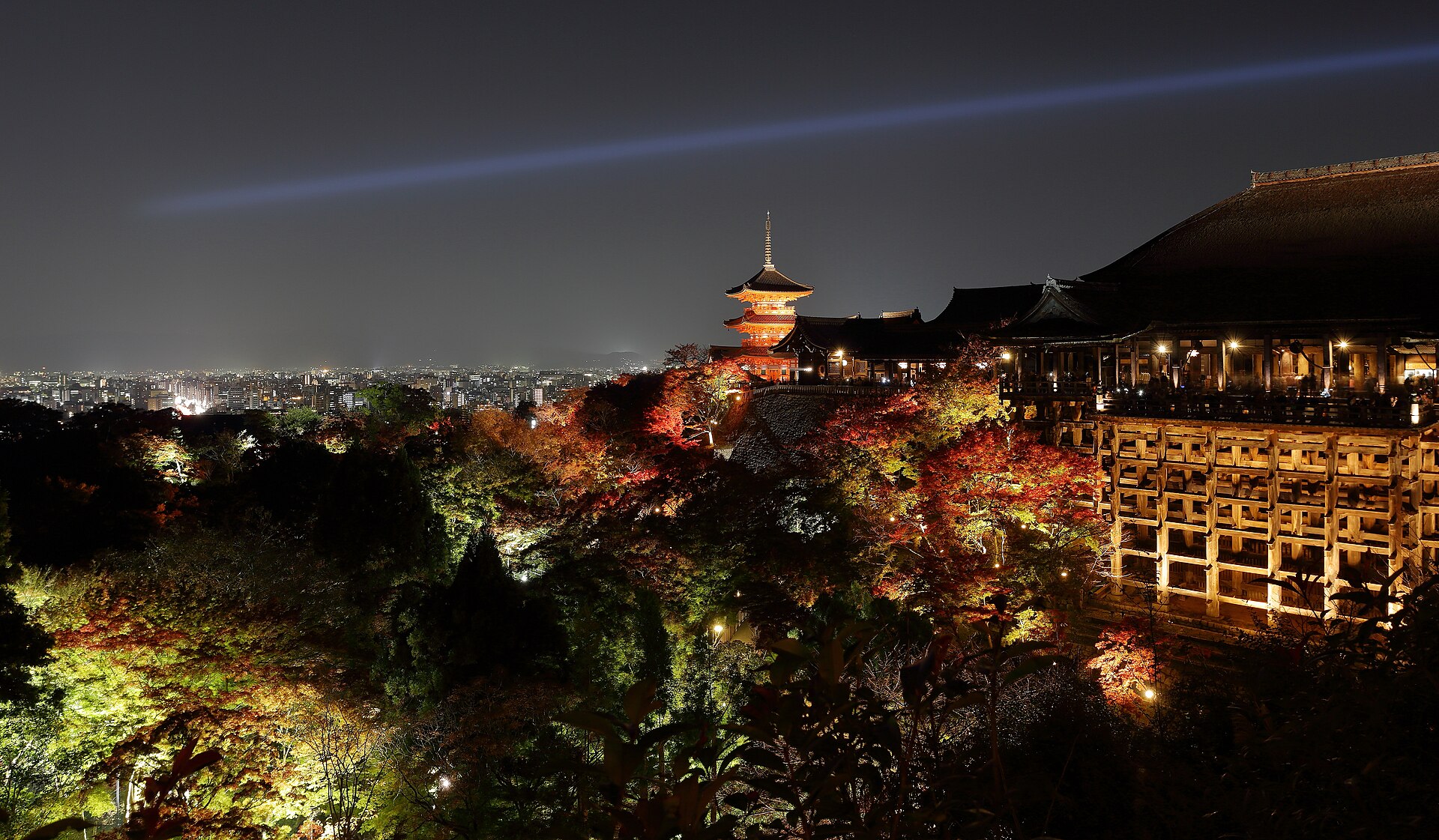 Kiyomizu-dera temple in Kyoto seen from the hillside, its wooden stage standing on tall pillars above autumn trees.