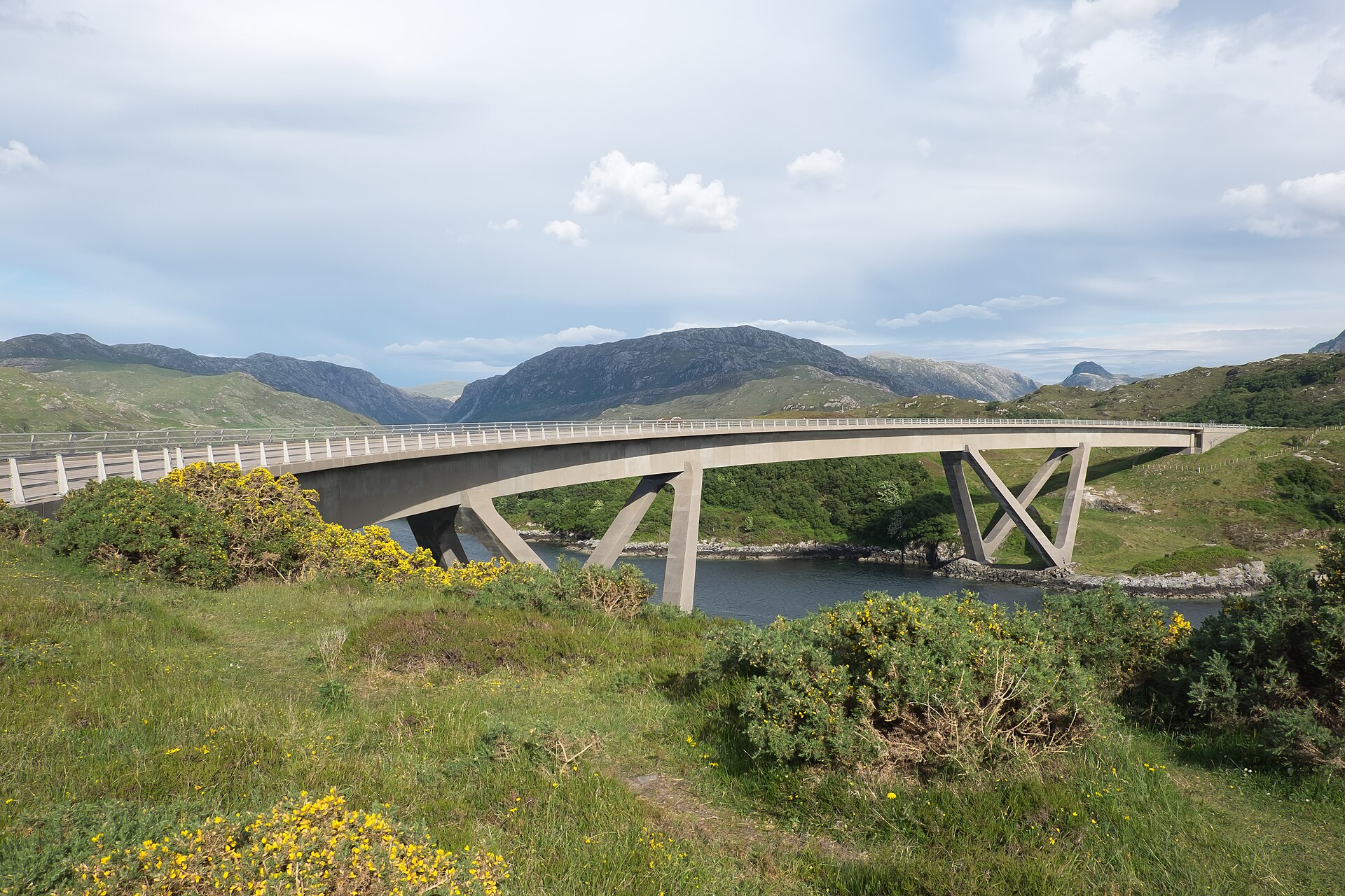 The curved concrete Kylesku Bridge spanning a sea loch in Sutherland, Scotland, with bare hills rising behind it.