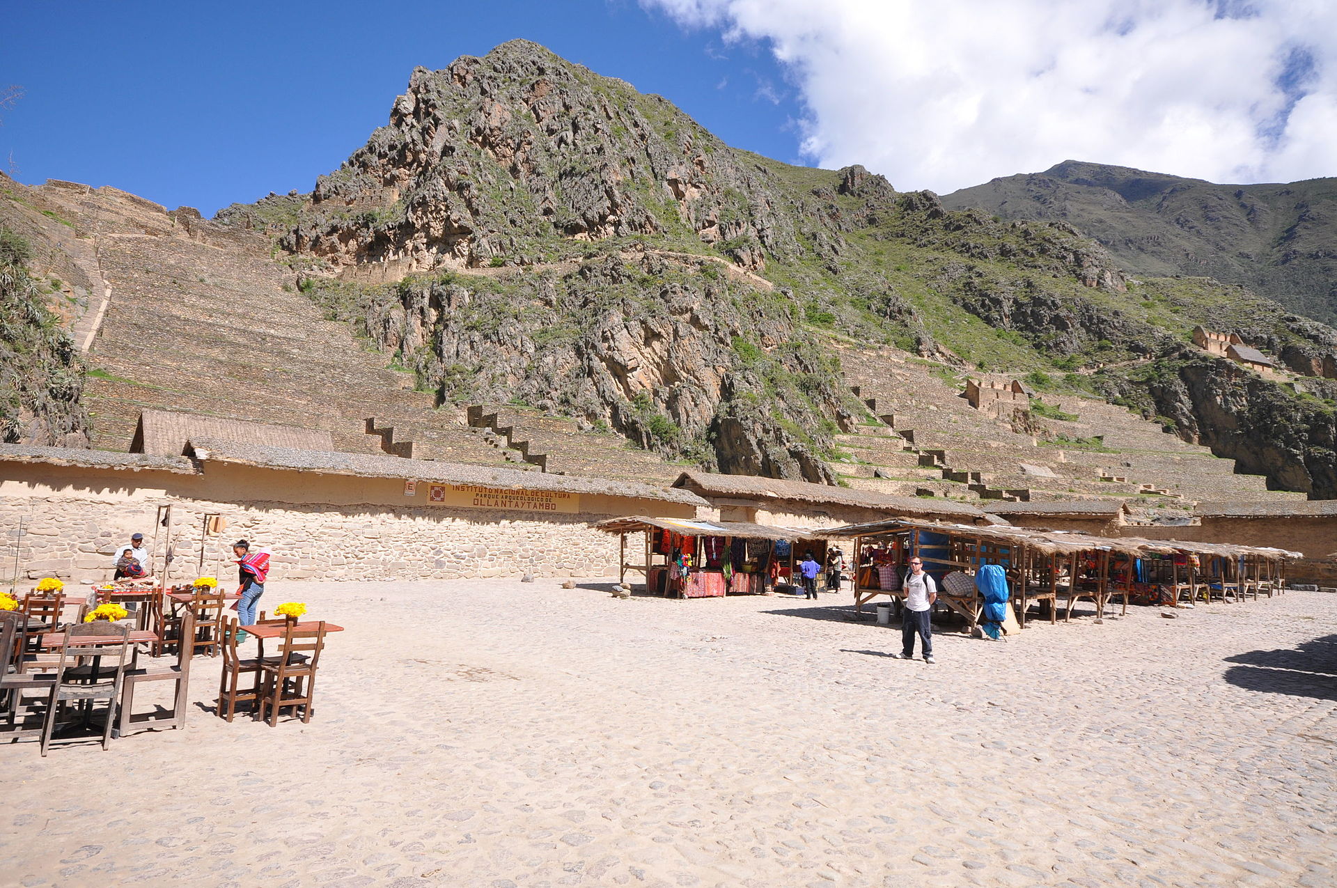 Steep stone agricultural terraces climbing the hillside above Ollantaytambo in Peru's Sacred Valley, with the valley floor and mountains behind.