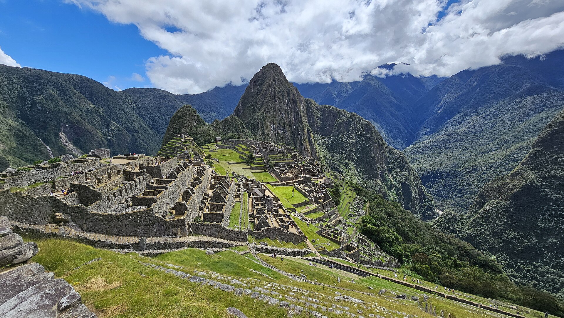 The Inca citadel of Machu Picchu seen from above, with terraced stonework spread along the ridge and the peak of Huayna Picchu rising behind it.