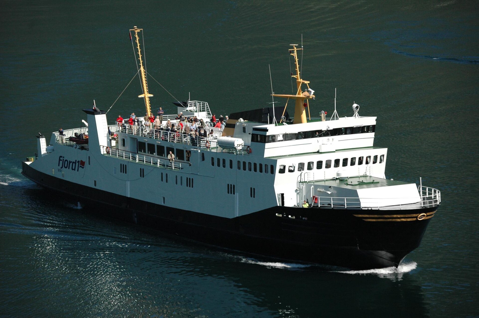 A white and red car ferry sailing on the Geirangerfjord in Norway between steep dark mountainsides.