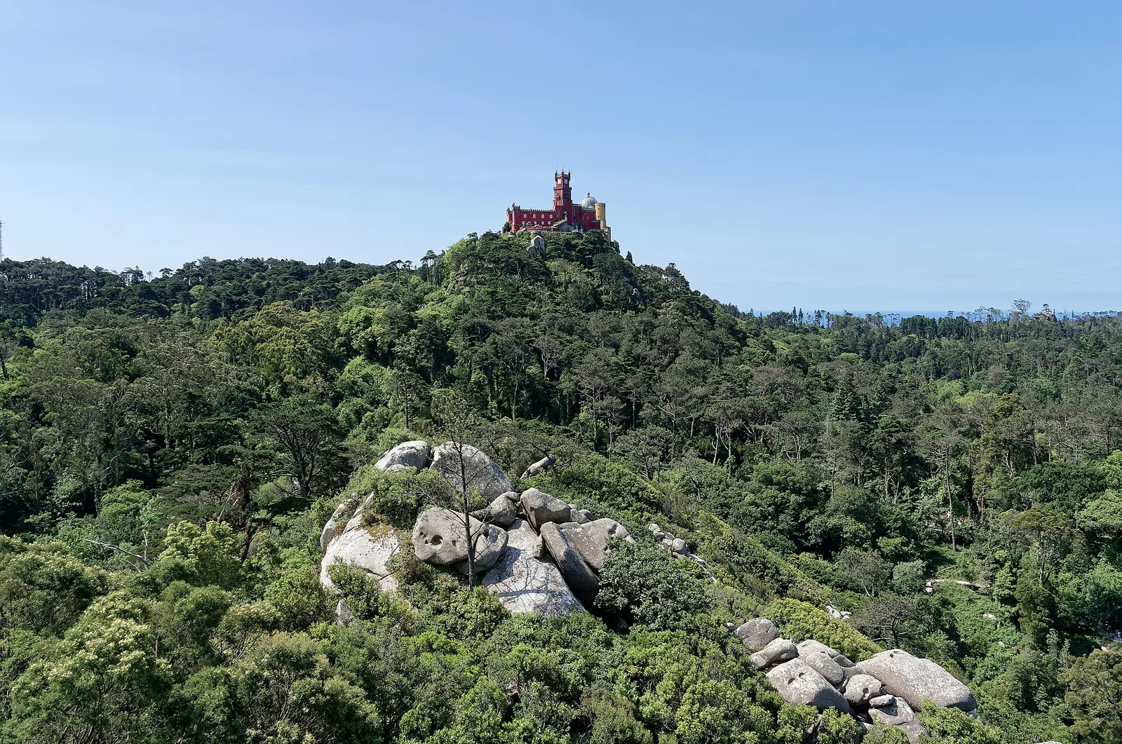 The brightly coloured Pena Palace on a wooded hilltop in Sintra, Portugal, seen from the Moorish castle walls.