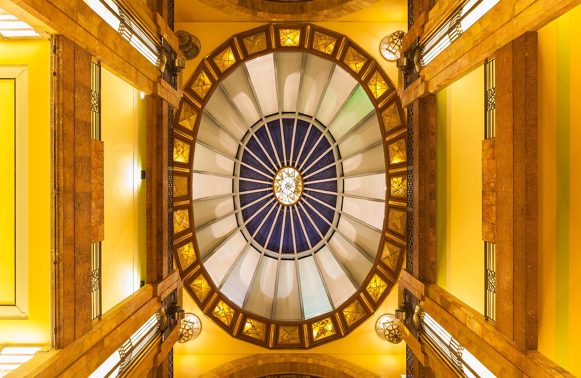 The stained glass and gilded interior dome of the Palacio de Bellas Artes in Mexico City, seen looking upwards from the floor below.