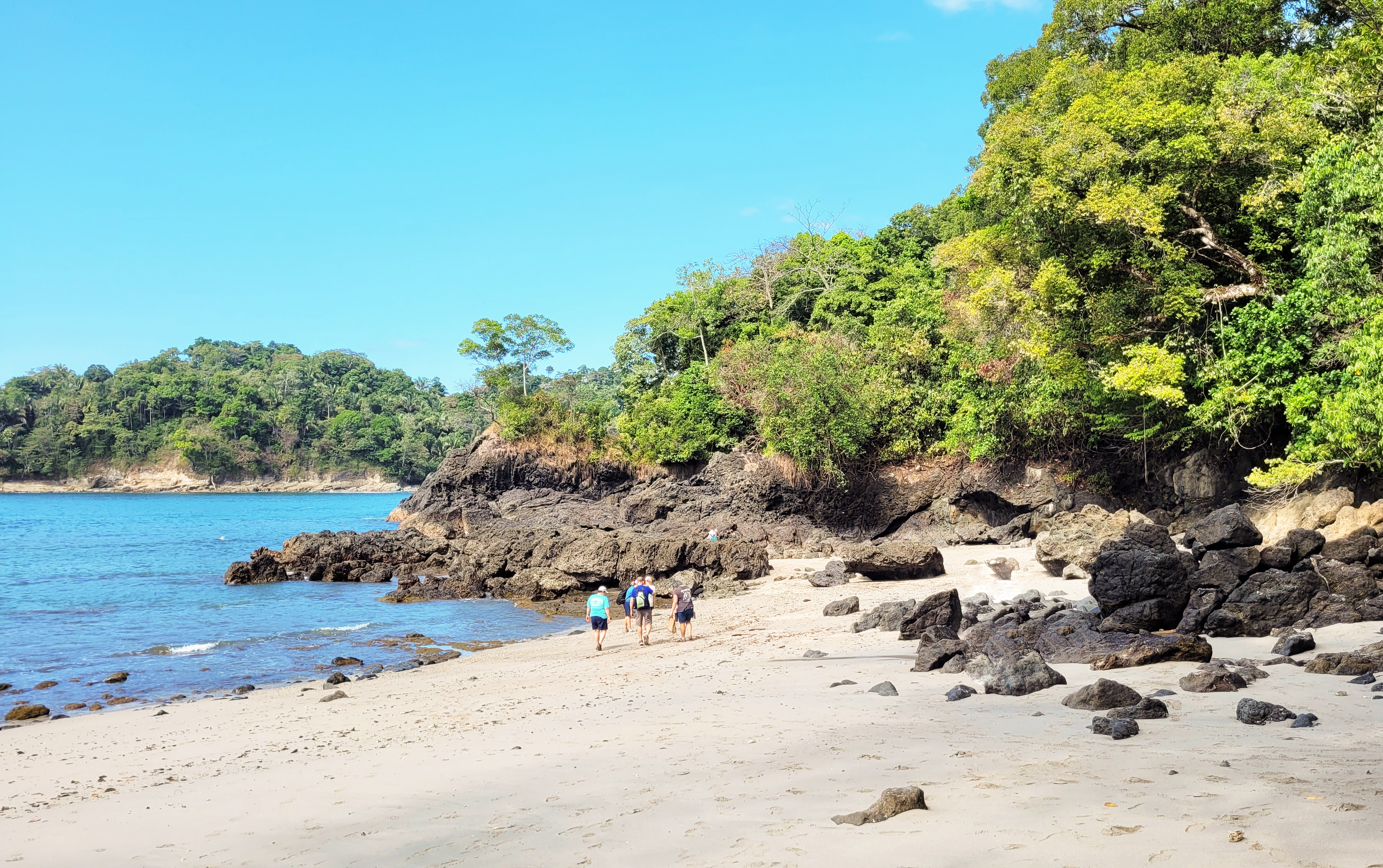 A beach inside Manuel Antonio National Park, pale sand meeting calm water with forest running to the shoreline.