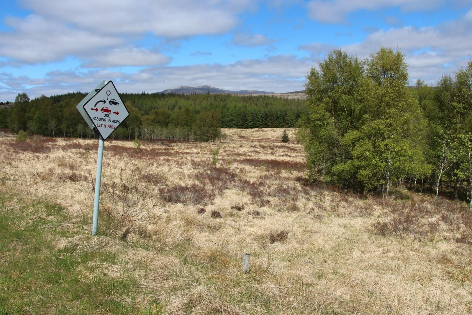 A white passing place sign on a post beside a single-track road running through open moorland in Strath Tirry, Sutherland, Scotland.