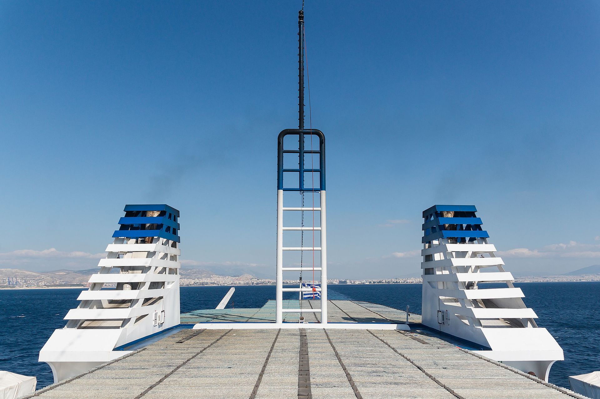 The port of Piraeus in Athens seen from the deck of a departing ferry, with the harbour front and the city rising behind it.