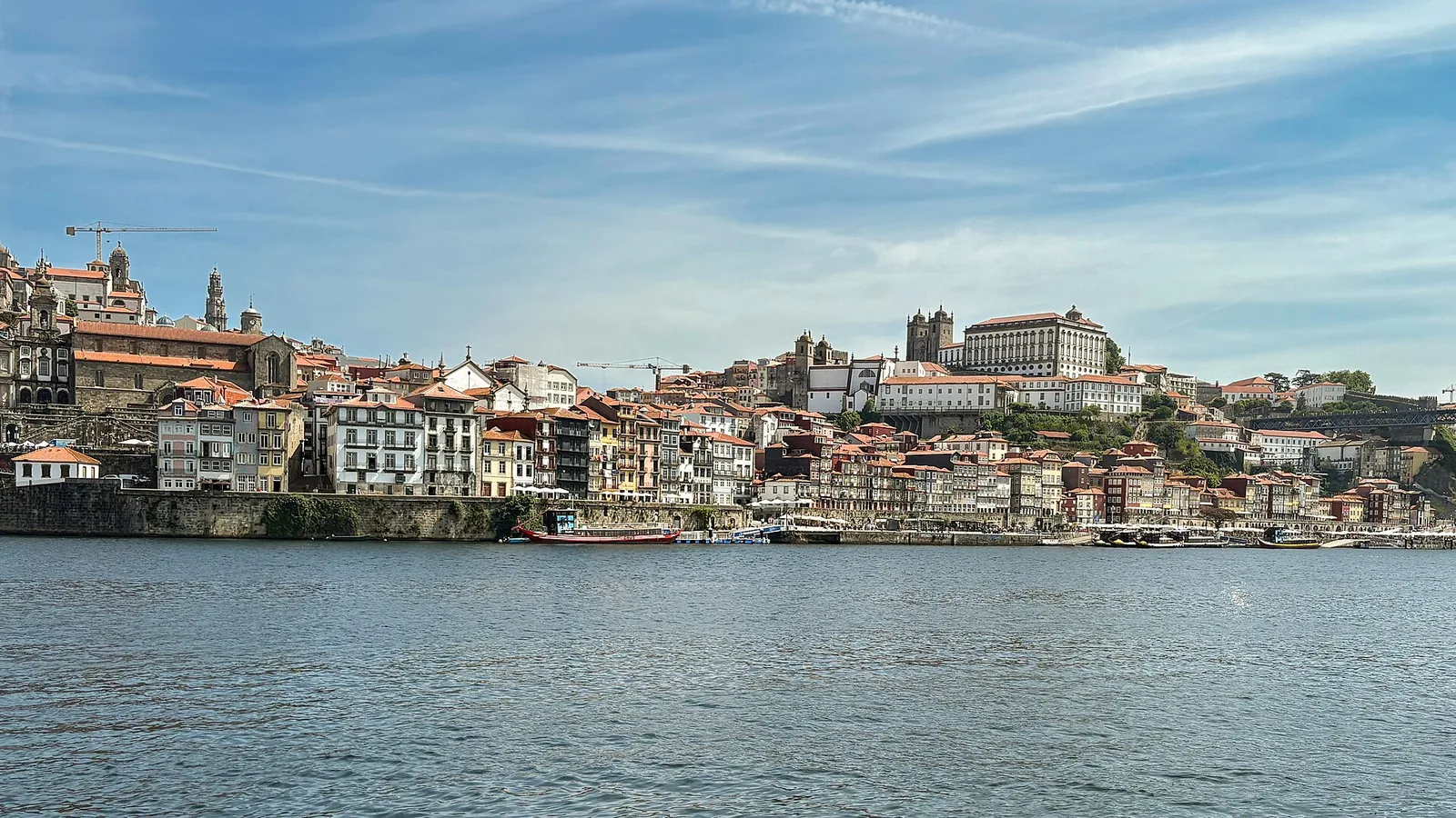 The Ribeira waterfront in Porto seen from across the Douro river, with pastel buildings stacked up the hillside and the cathedral above.