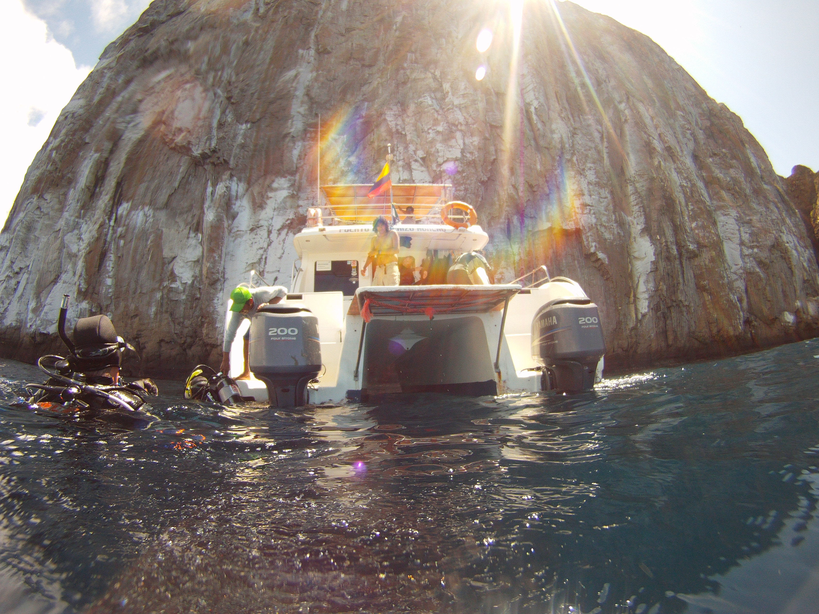 A dive boat anchored beneath the towering rock walls of Kicker Rock (Leon Dormido), divers preparing to enter the water near San Cristobal Island.