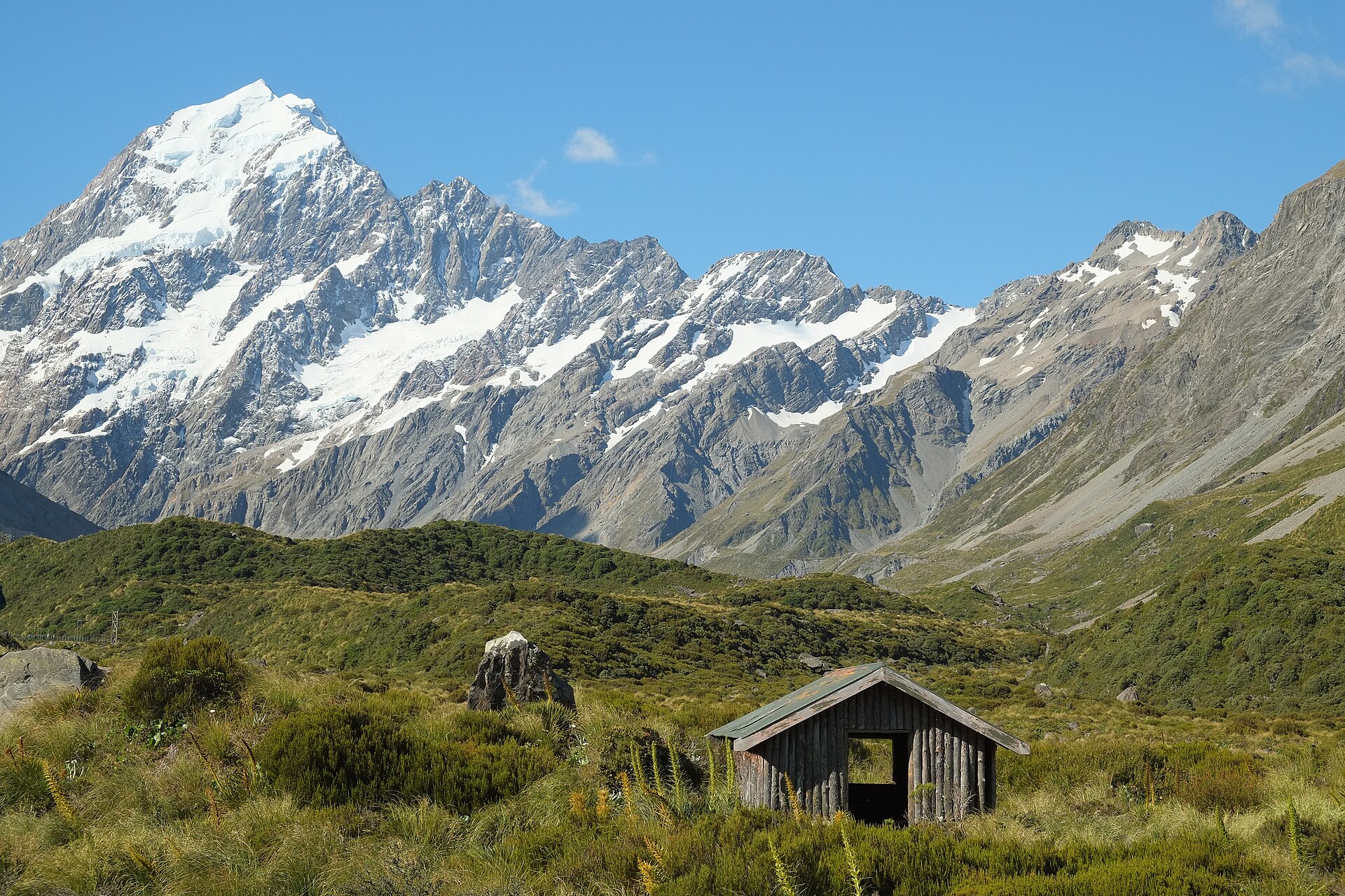 A small shelter beside the gravel Hooker Valley Track in Aoraki/Mount Cook National Park, New Zealand, with the snow-covered Mount Cook Range rising behind.