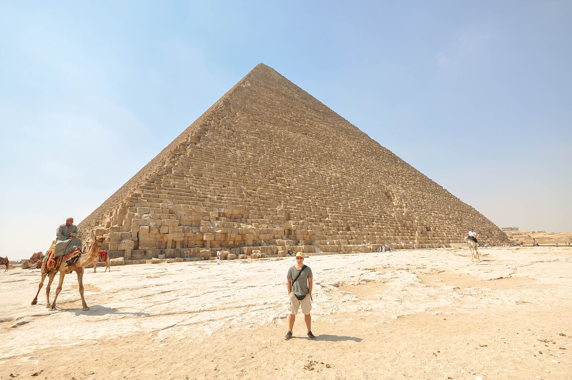 The Great Pyramid of Giza seen from close to its base, the eroded limestone blocks rising in stepped courses against a clear sky.