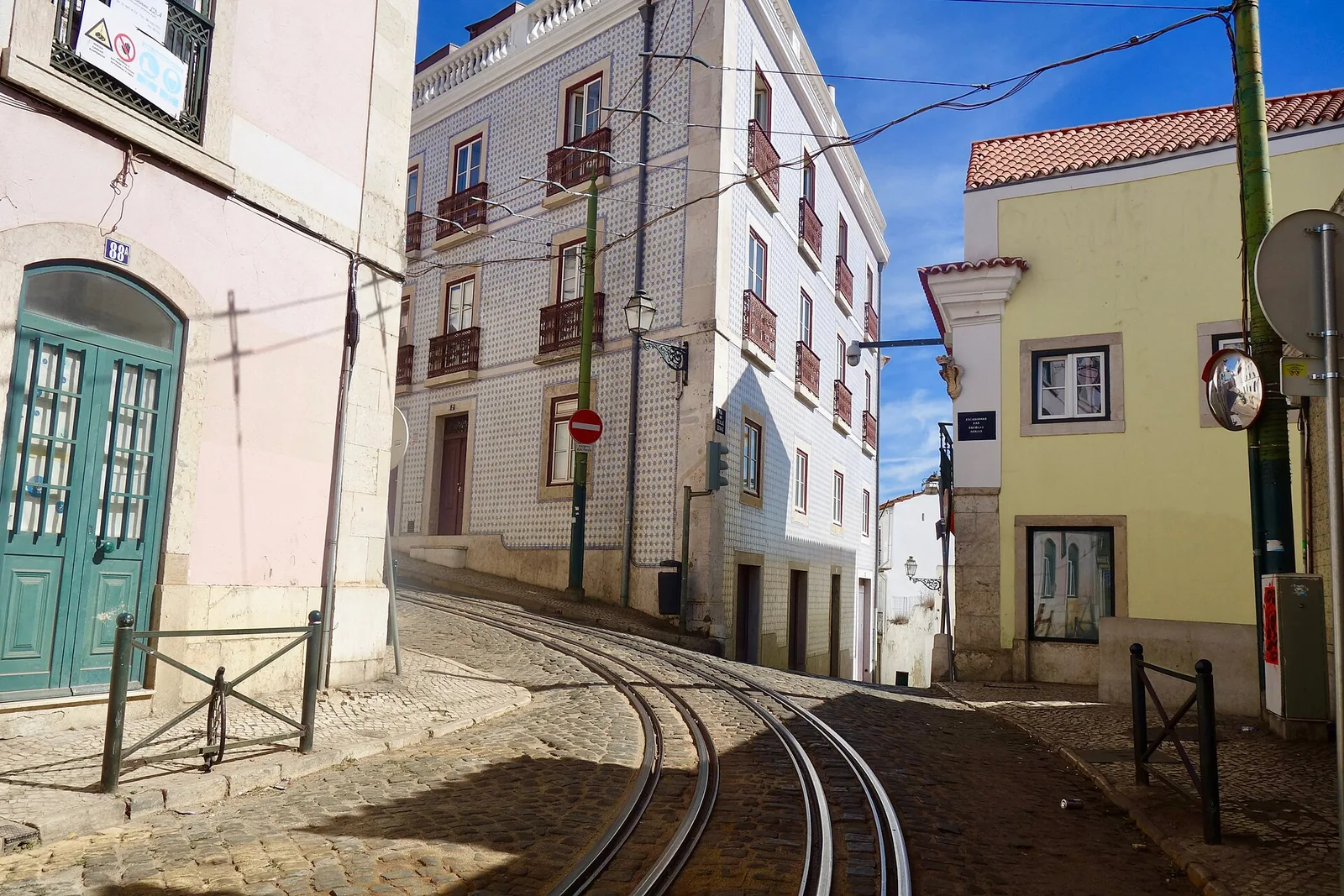 A yellow tram on line 28 climbing a narrow street in the Alfama district of Lisbon between tiled buildings.
