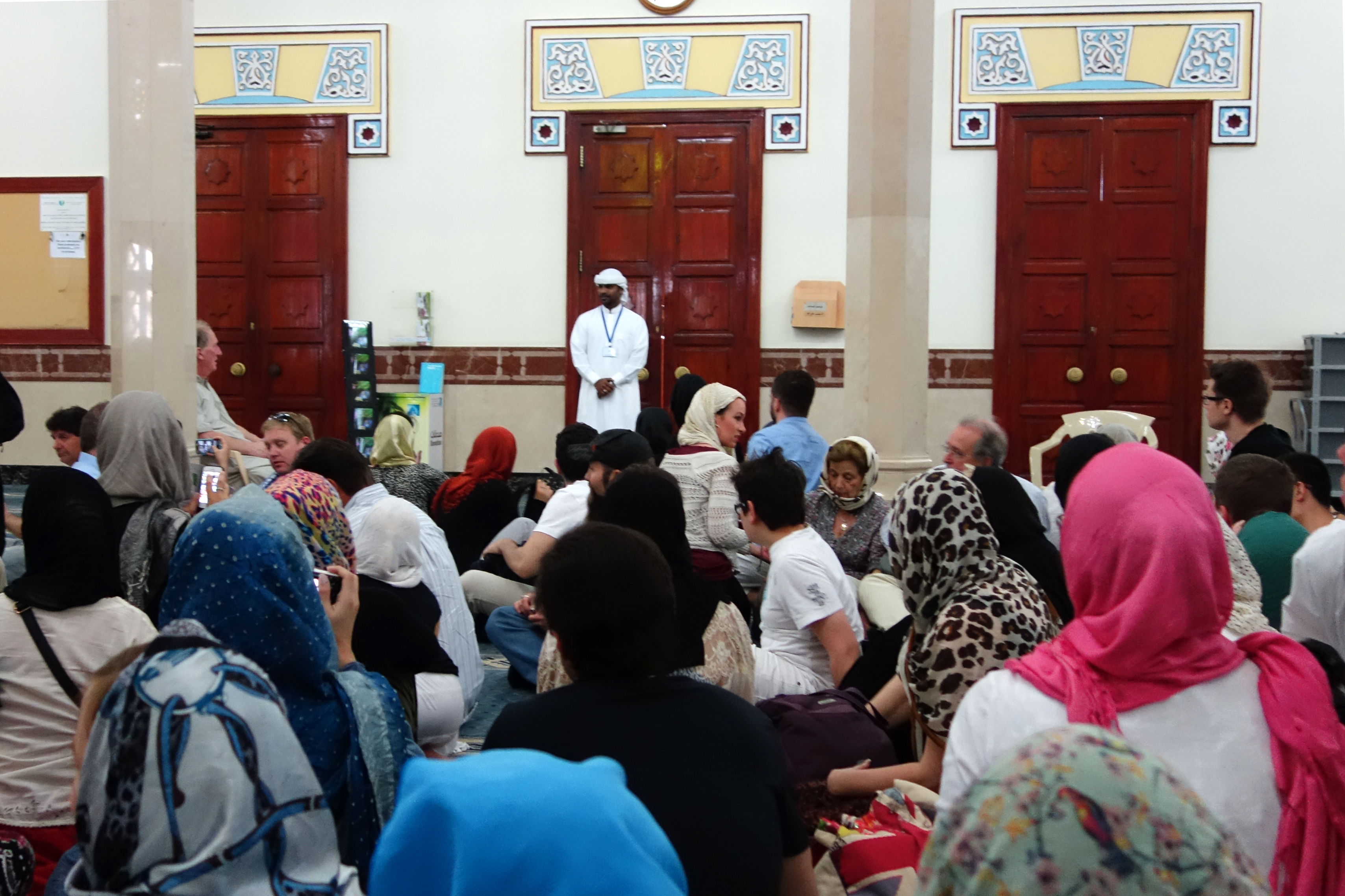 Visitors sitting inside Jumeirah Mosque in Dubai, listening to a guide during a cultural tour.