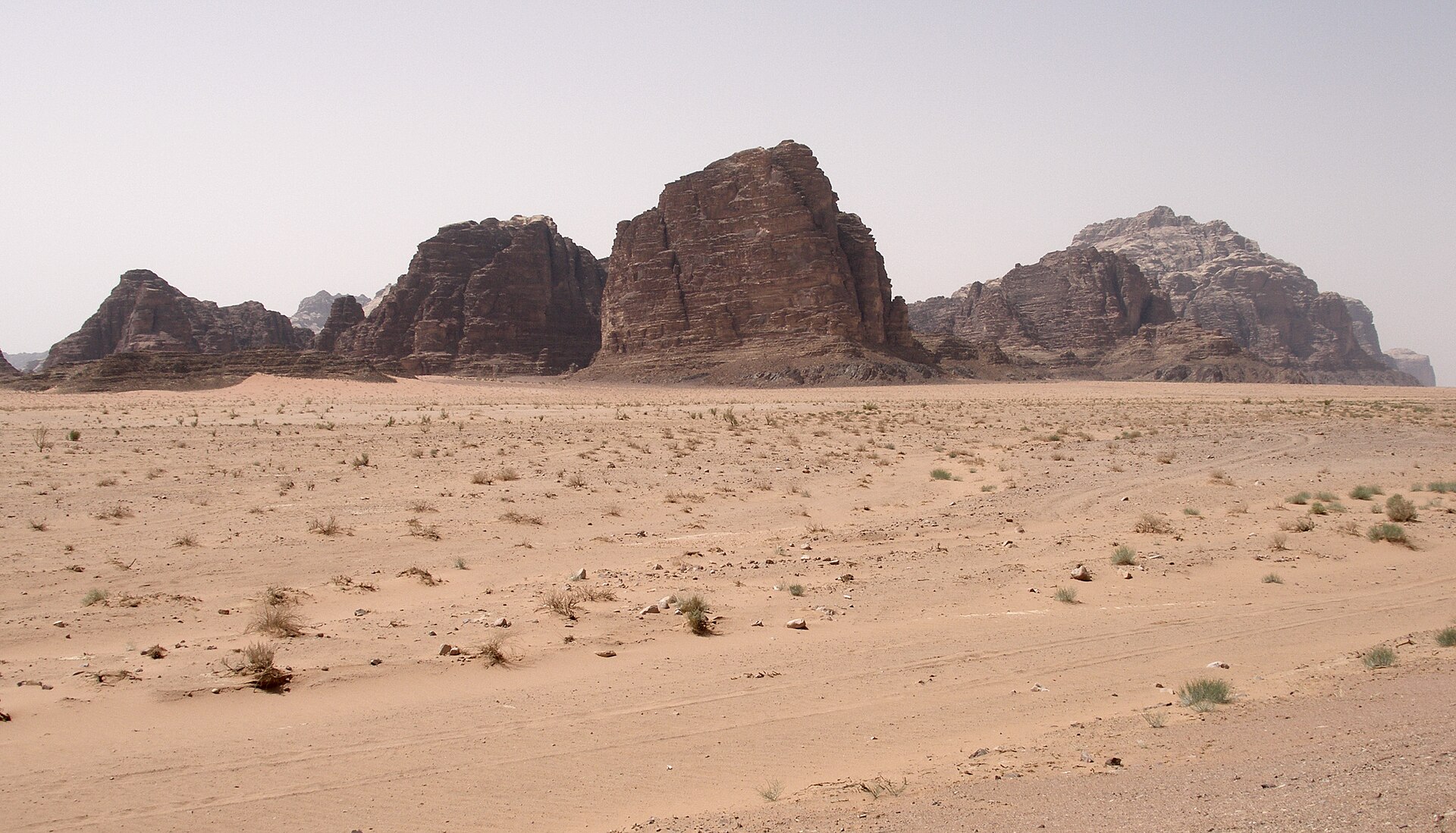 The open desert of Wadi Rum in southern Jordan, with sandstone massifs rising out of red sand under a clear sky.